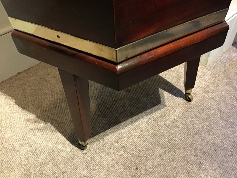 A hexagonal dark mahogany Georgian wine cooler featuring brass binding straps, side handles, and tapered legs on brass castors. View IV