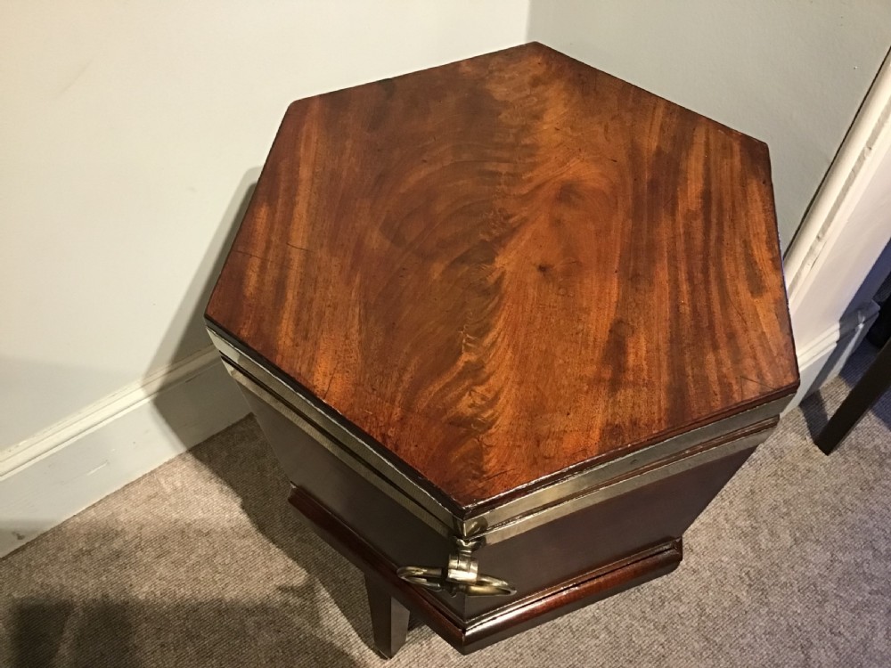 A hexagonal dark mahogany Georgian wine cooler featuring brass binding straps, side handles, and tapered legs on brass castors. View VI