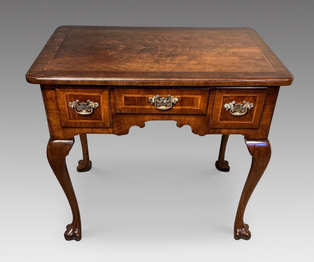 A Georgian walnut lowboy featuring three drawers with brass handles, a crossbanded veneered top, a shaped apron, and four cabriole legs with pad feet.