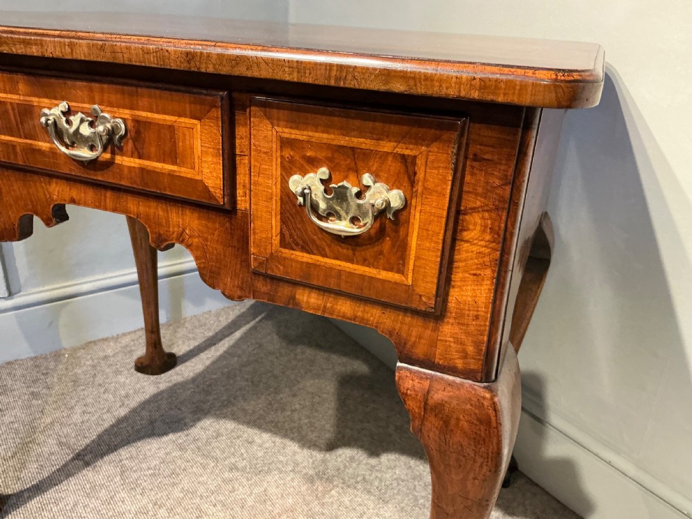 A Georgian walnut lowboy featuring three drawers with brass handles, a crossbanded veneered top, a shaped apron, and four cabriole legs with pad feet. View II