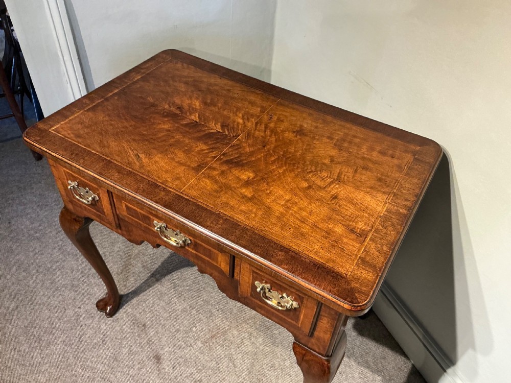 A Georgian walnut lowboy featuring three drawers with brass handles, a crossbanded veneered top, a shaped apron, and four cabriole legs with pad feet. View III