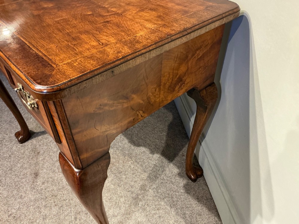 A Georgian walnut lowboy featuring three drawers with brass handles, a crossbanded veneered top, a shaped apron, and four cabriole legs with pad feet. View IV