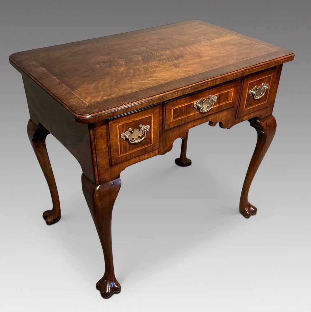 A Georgian walnut lowboy featuring three drawers with brass handles, a crossbanded veneered top, a shaped apron, and four cabriole legs with pad feet. View V
