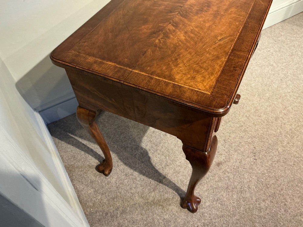 A Georgian walnut lowboy featuring three drawers with brass handles, a crossbanded veneered top, a shaped apron, and four cabriole legs with pad feet. View VIII