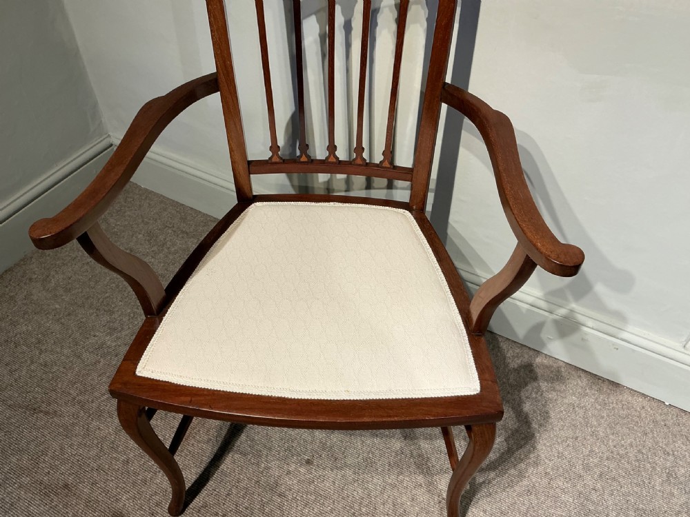 An Edwardian mahogany elbow chair featuring a cream upholstered seat and upper back panel, inlaid vertical splats, curved arms, and cabriole front legs. View II