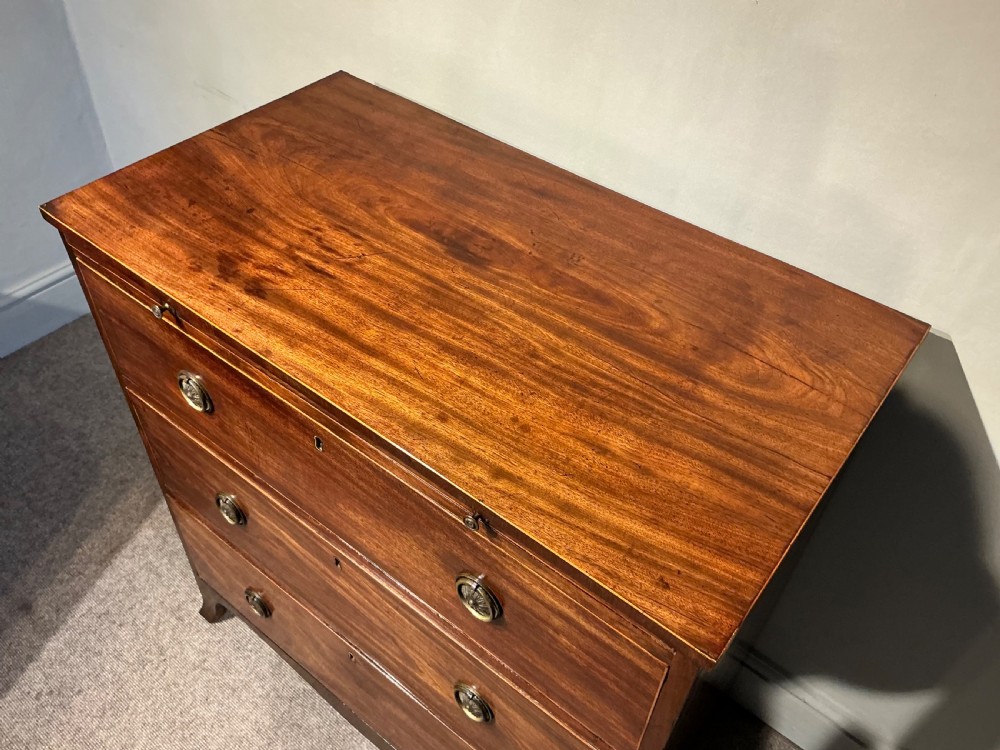 A Georgian mahogany chest of drawers featuring three graduated drawers, a pull-out brushing slide, brass rosette handles, and splayed bracket feet. View III