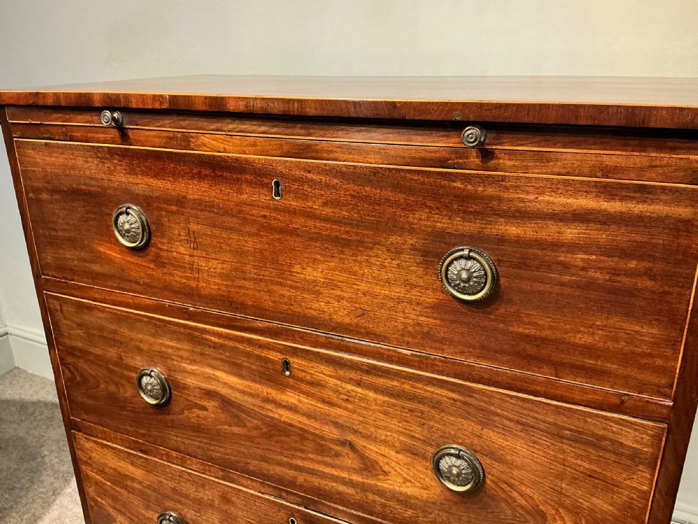 A Georgian mahogany chest of drawers featuring three graduated drawers, a pull-out brushing slide, brass rosette handles, and splayed bracket feet. View V
