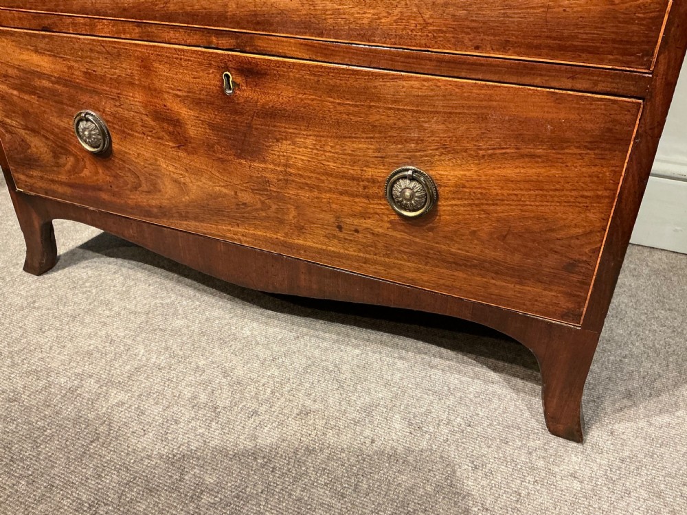 A Georgian mahogany chest of drawers featuring three graduated drawers, a pull-out brushing slide, brass rosette handles, and splayed bracket feet. View VI