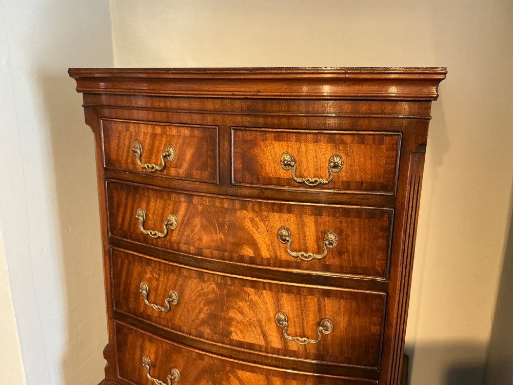 A tall mahogany bowfront chest of drawers featuring flame timber veneers, brass swan-neck handles, and bracket feet. View II