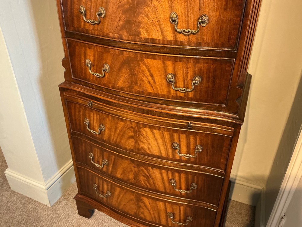 A tall mahogany bowfront chest of drawers featuring flame timber veneers, brass swan-neck handles, and bracket feet. View III