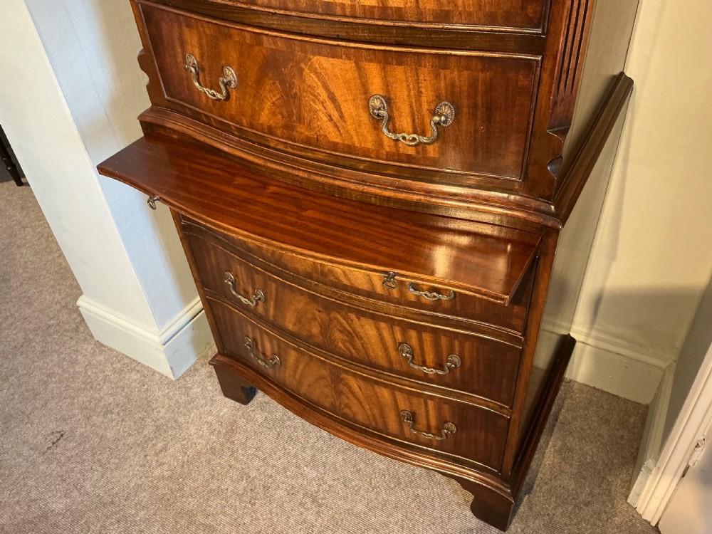 A tall mahogany bowfront chest of drawers featuring flame timber veneers, brass swan-neck handles, and bracket feet. View VI