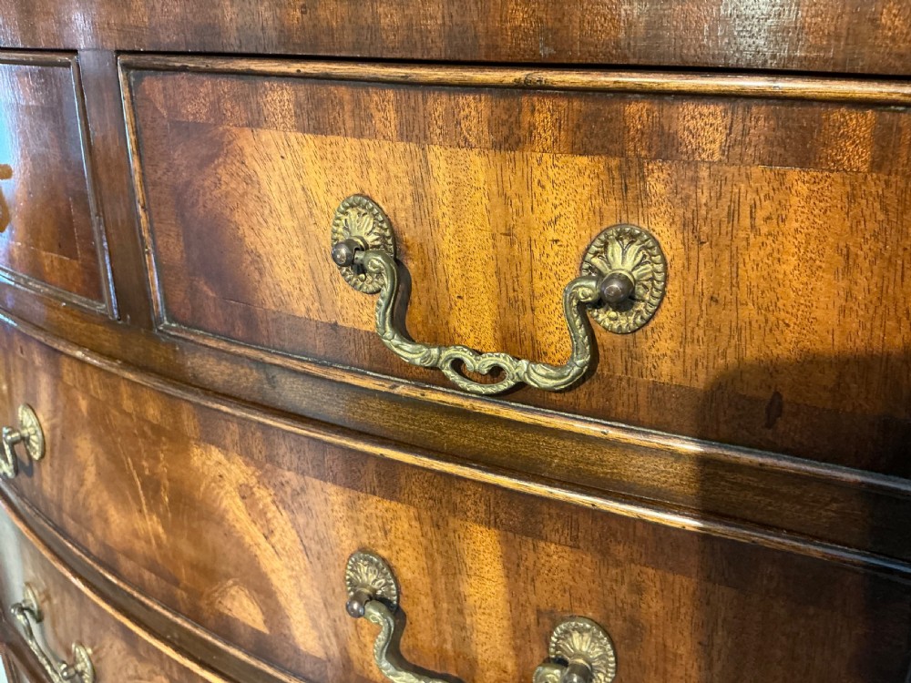 A tall mahogany bowfront chest of drawers featuring flame timber veneers, brass swan-neck handles, and bracket feet. View VII