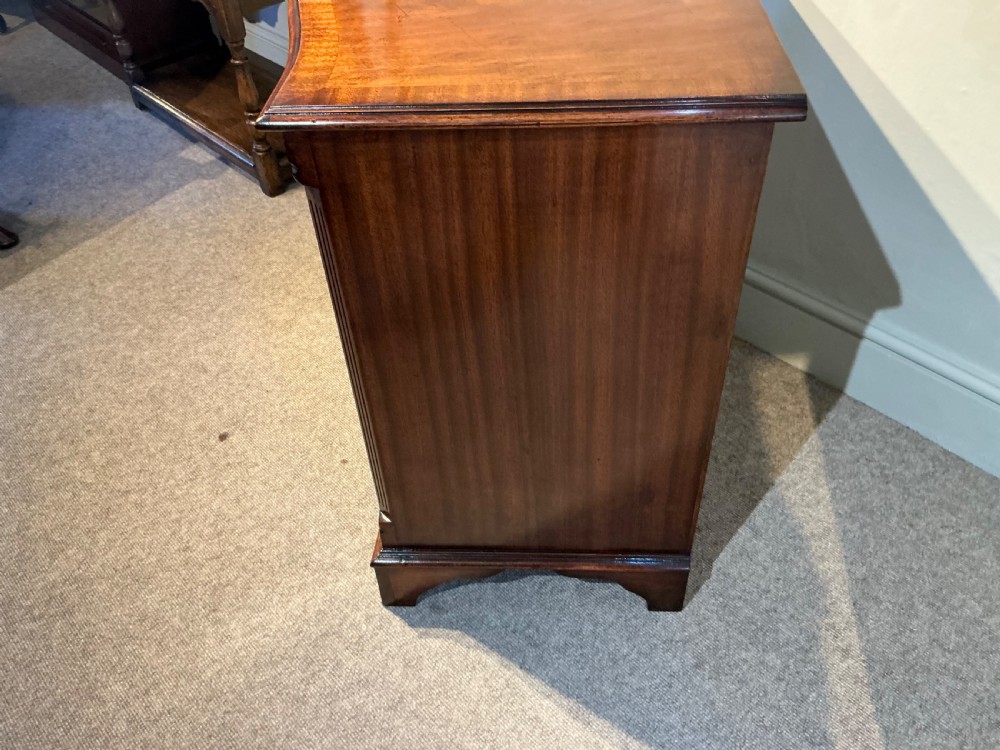 A Georgian mahogany serpentine chest of drawers featuring four graduated drawers with brass swan-neck handles and bracket feet. View V