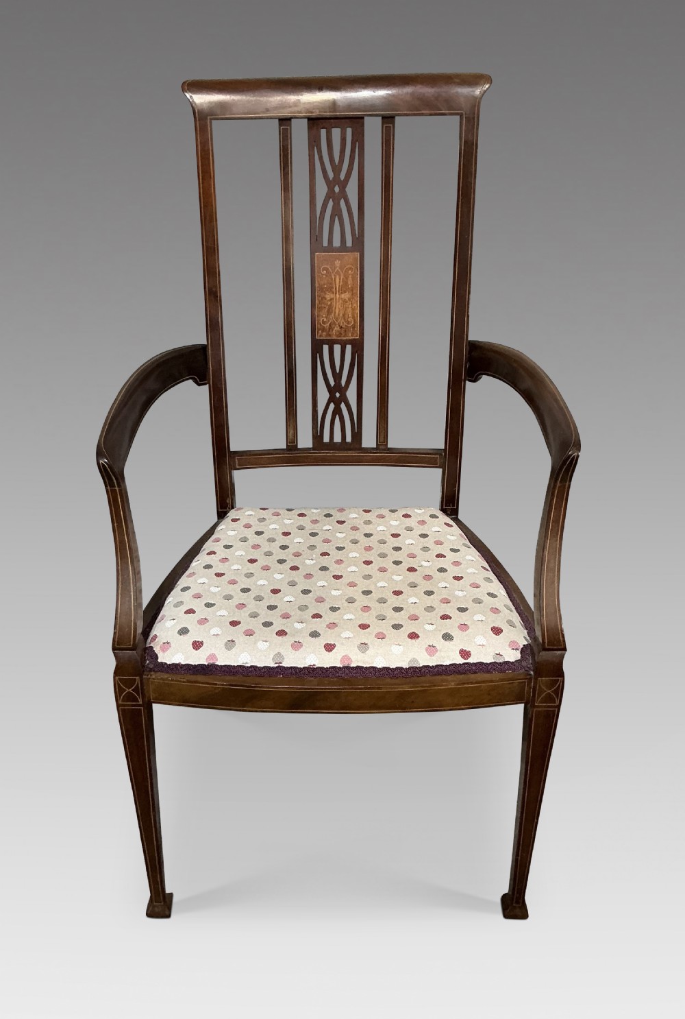 An Edwardian mahogany elbow chair featuring a central pierced splat with satinwood marquetry, swept armrests, and a patterned fabric seat.