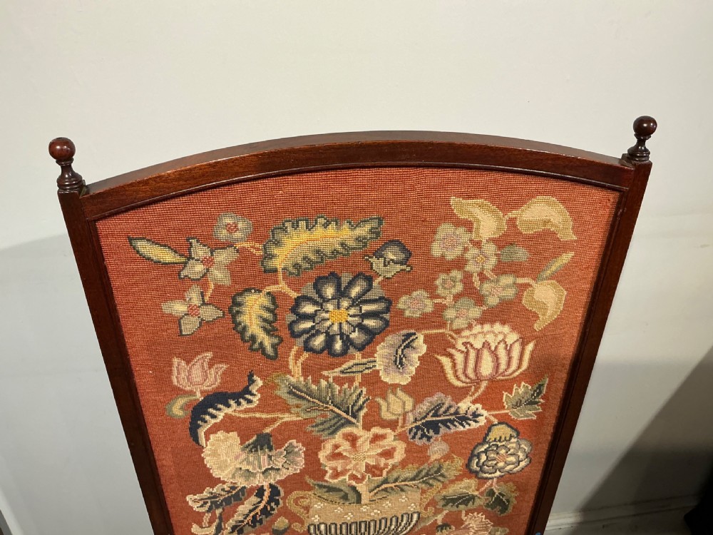 A 19th-century dark wooden fire screen featuring a floral needlepoint panel set on a terracotta background. View II