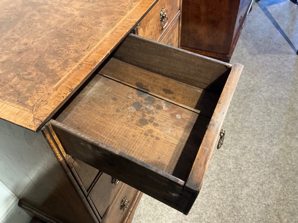 An antique burr walnut chest of drawers featuring two short over three long graduating drawers with brass handles and bracket feet. View V