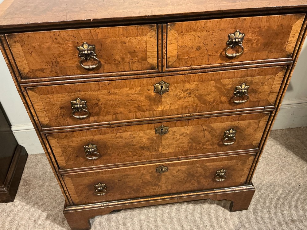 An antique burr walnut chest of drawers featuring two short over three long graduating drawers with brass handles and bracket feet. View VI