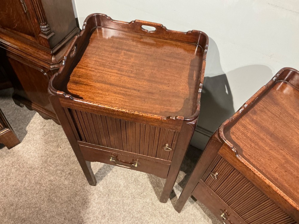 A pair of antique dark mahogany bedside cabinets featuring tray tops with carved handles, slatted tambour sliding doors, single drawers with brass handles, and square legs. View IV