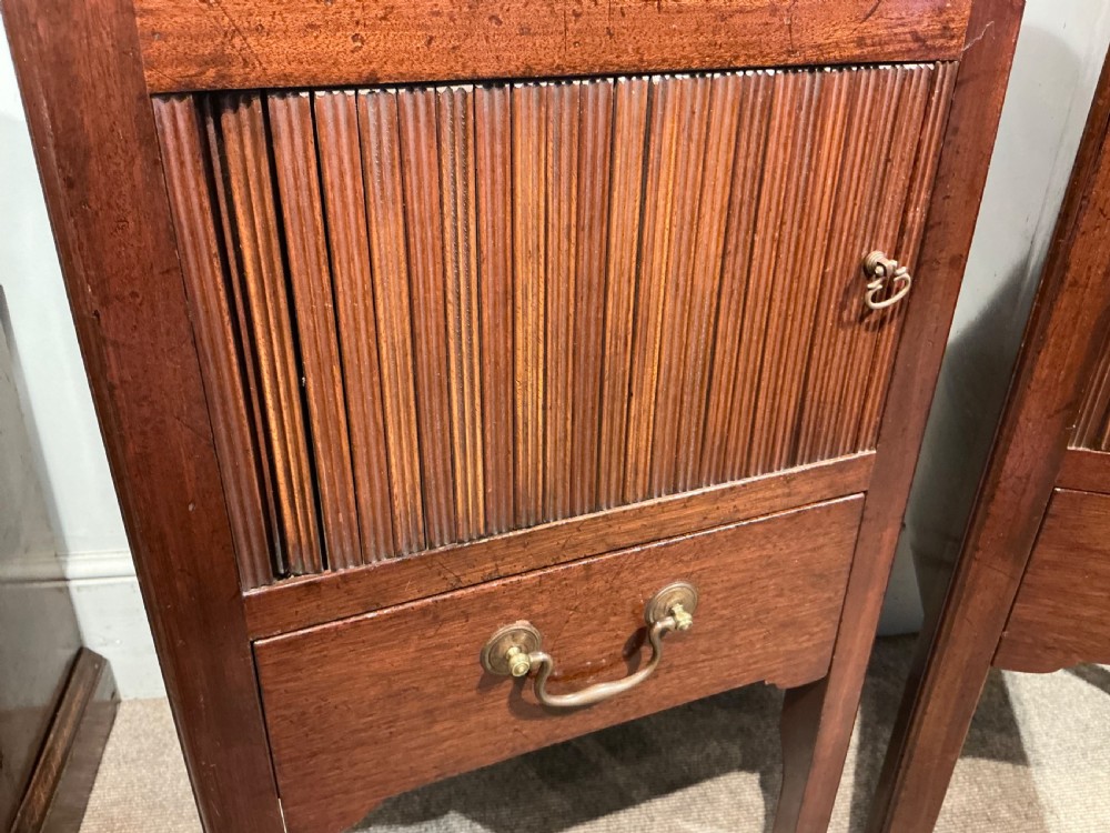 A pair of antique dark mahogany bedside cabinets featuring tray tops with carved handles, slatted tambour sliding doors, single drawers with brass handles, and square legs. View V