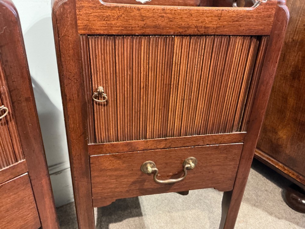 A pair of antique dark mahogany bedside cabinets featuring tray tops with carved handles, slatted tambour sliding doors, single drawers with brass handles, and square legs. View VI