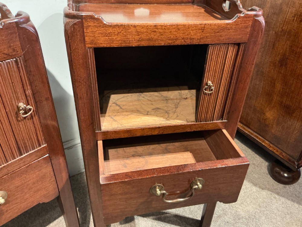 A pair of antique dark mahogany bedside cabinets featuring tray tops with carved handles, slatted tambour sliding doors, single drawers with brass handles, and square legs. View VII