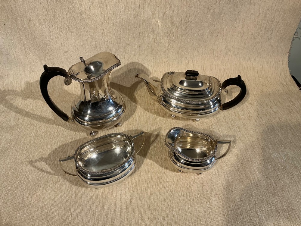 A four-piece antique silver-plated tea service comprising a teapot, coffee pot, sugar bowl, and milk jug with carved dark wood handles and ball feet.