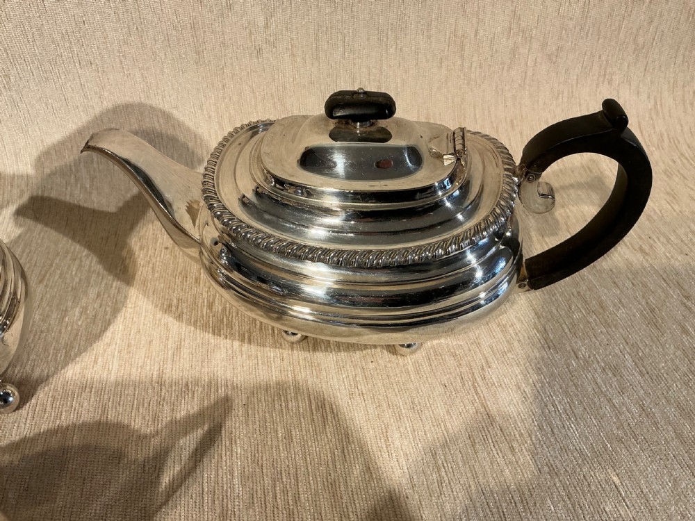 A four-piece antique silver-plated tea service comprising a teapot, coffee pot, sugar bowl, and milk jug with carved dark wood handles and ball feet. View II