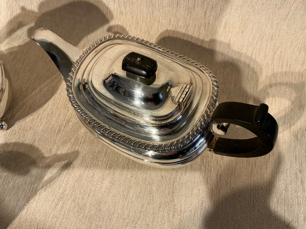 A four-piece antique silver-plated tea service comprising a teapot, coffee pot, sugar bowl, and milk jug with carved dark wood handles and ball feet. View III