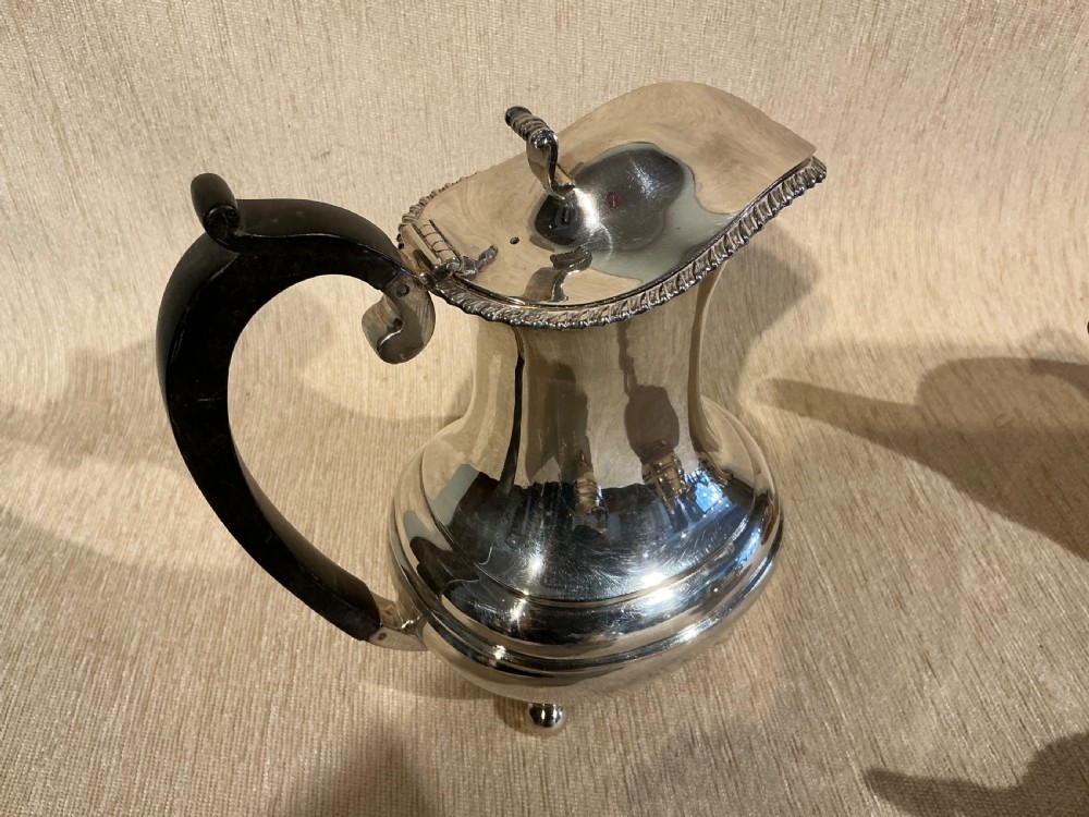 A four-piece antique silver-plated tea service comprising a teapot, coffee pot, sugar bowl, and milk jug with carved dark wood handles and ball feet. View IV