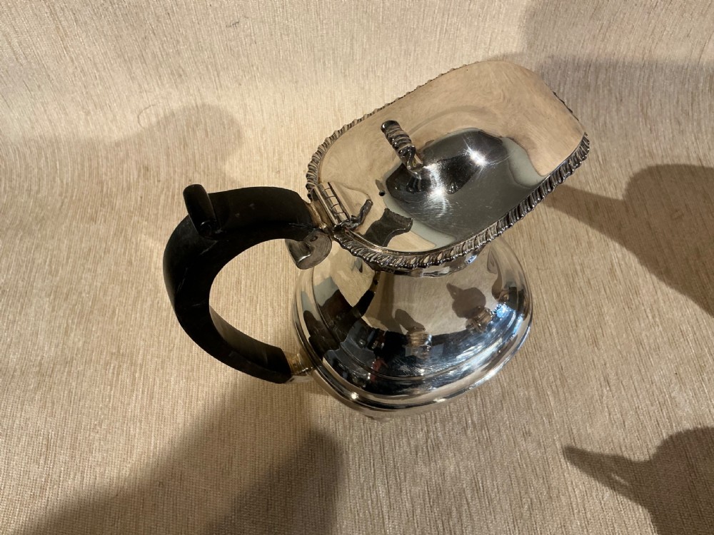 A four-piece antique silver-plated tea service comprising a teapot, coffee pot, sugar bowl, and milk jug with carved dark wood handles and ball feet. View V