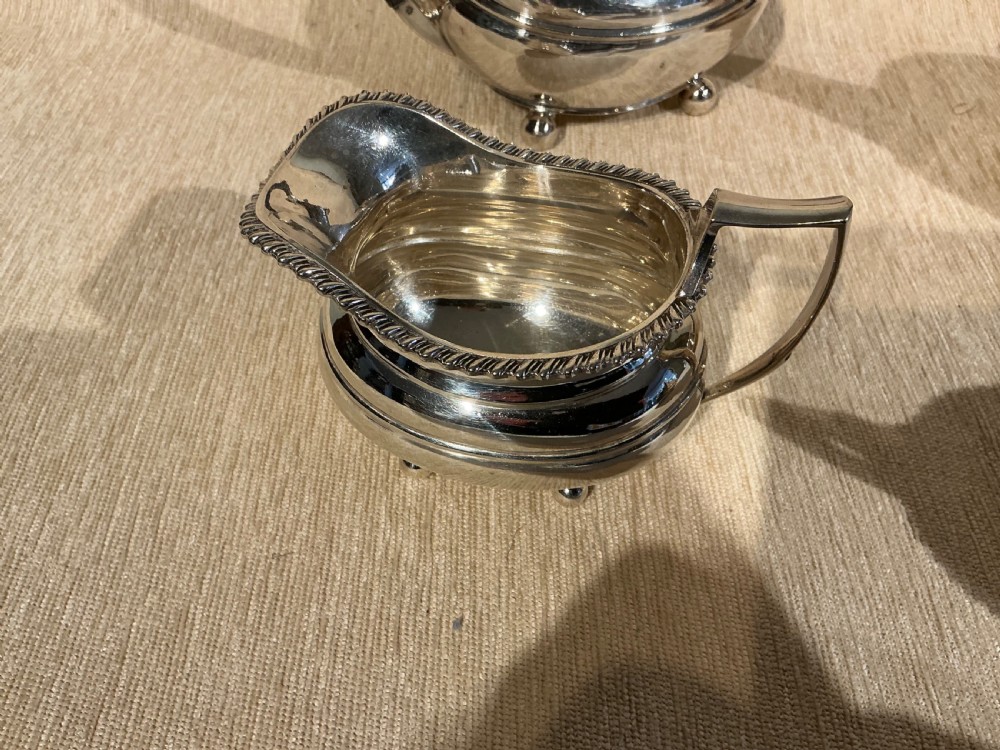 A four-piece antique silver-plated tea service comprising a teapot, coffee pot, sugar bowl, and milk jug with carved dark wood handles and ball feet. View VI