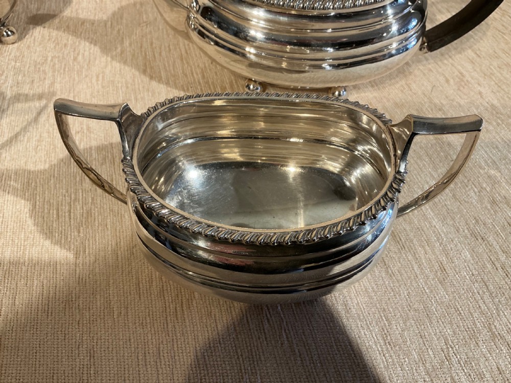 A four-piece antique silver-plated tea service comprising a teapot, coffee pot, sugar bowl, and milk jug with carved dark wood handles and ball feet. View VII