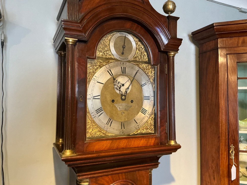 An antique Georgian longcase clock crafted from dark flame mahogany, featuring an arched hood with brass finials and an engraved brass dial. View II