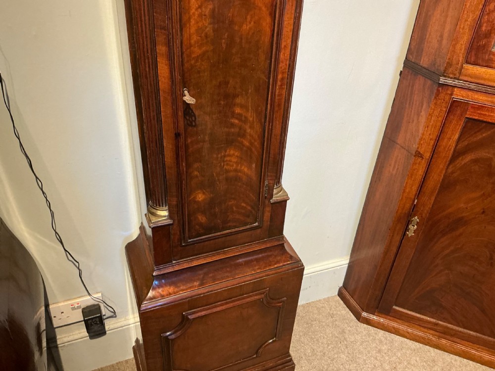 An antique Georgian longcase clock crafted from dark flame mahogany, featuring an arched hood with brass finials and an engraved brass dial. View III