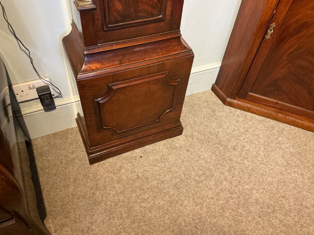 An antique Georgian longcase clock crafted from dark flame mahogany, featuring an arched hood with brass finials and an engraved brass dial. View V
