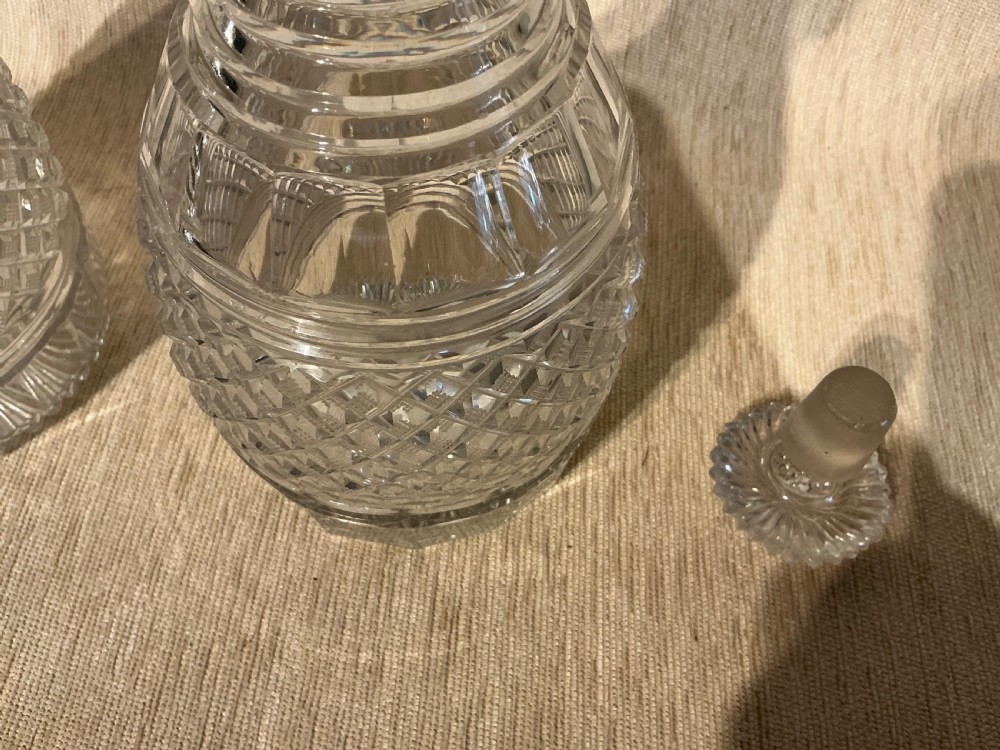 A pair of late Georgian clear cut-glass decanters featuring stepped neck rings, diamond pattern bands, and flat mushroom stoppers. View V