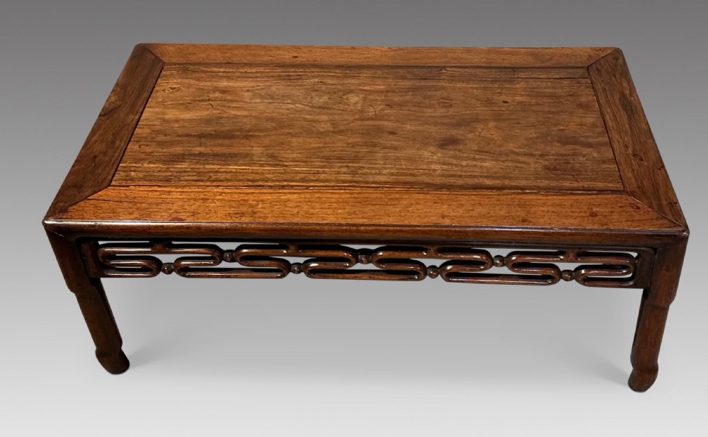 A low rectangular wooden Chinese opium table featuring a carved openwork apron and short inward-curving legs.
