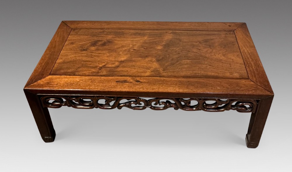 A low rectangular dark hardwood Chinese tea table featuring a mitred frame top, openwork carved scrollwork apron, and straight legs.