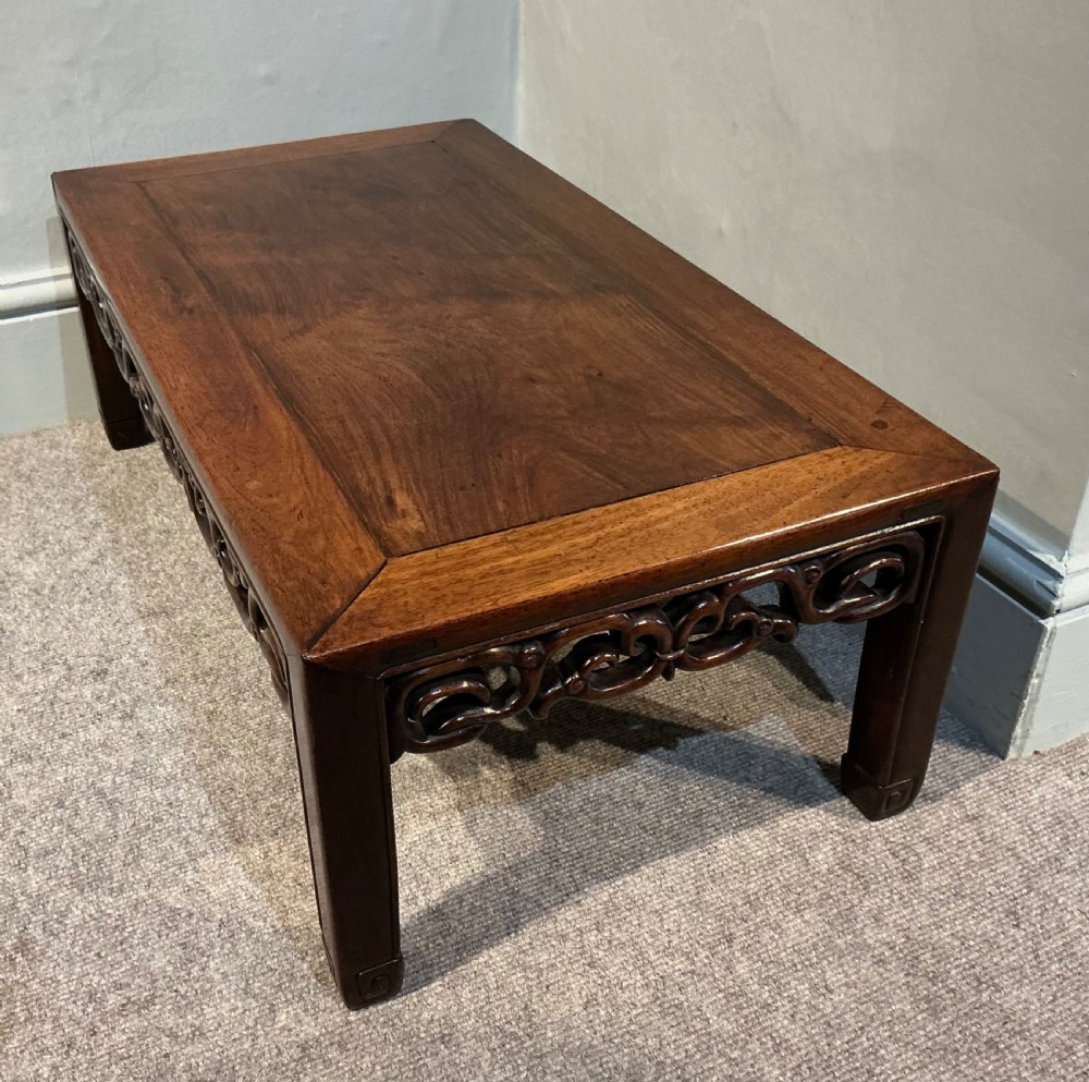 A low rectangular dark hardwood Chinese tea table featuring a mitred frame top, openwork carved scrollwork apron, and straight legs. View V