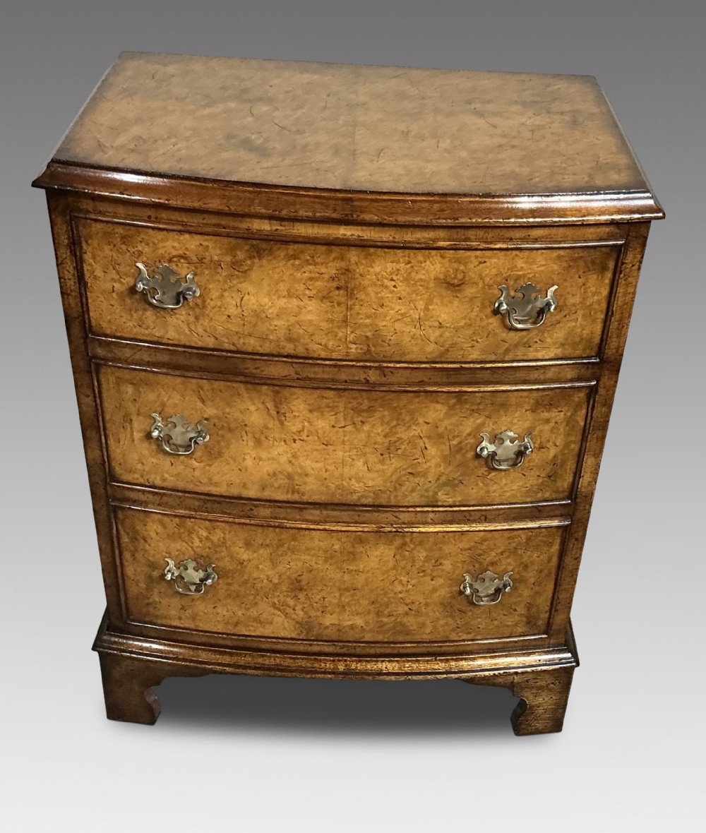 A burr walnut chest of drawers featuring three bow-fronted graduated drawers with brass swing handles and bracket feet.