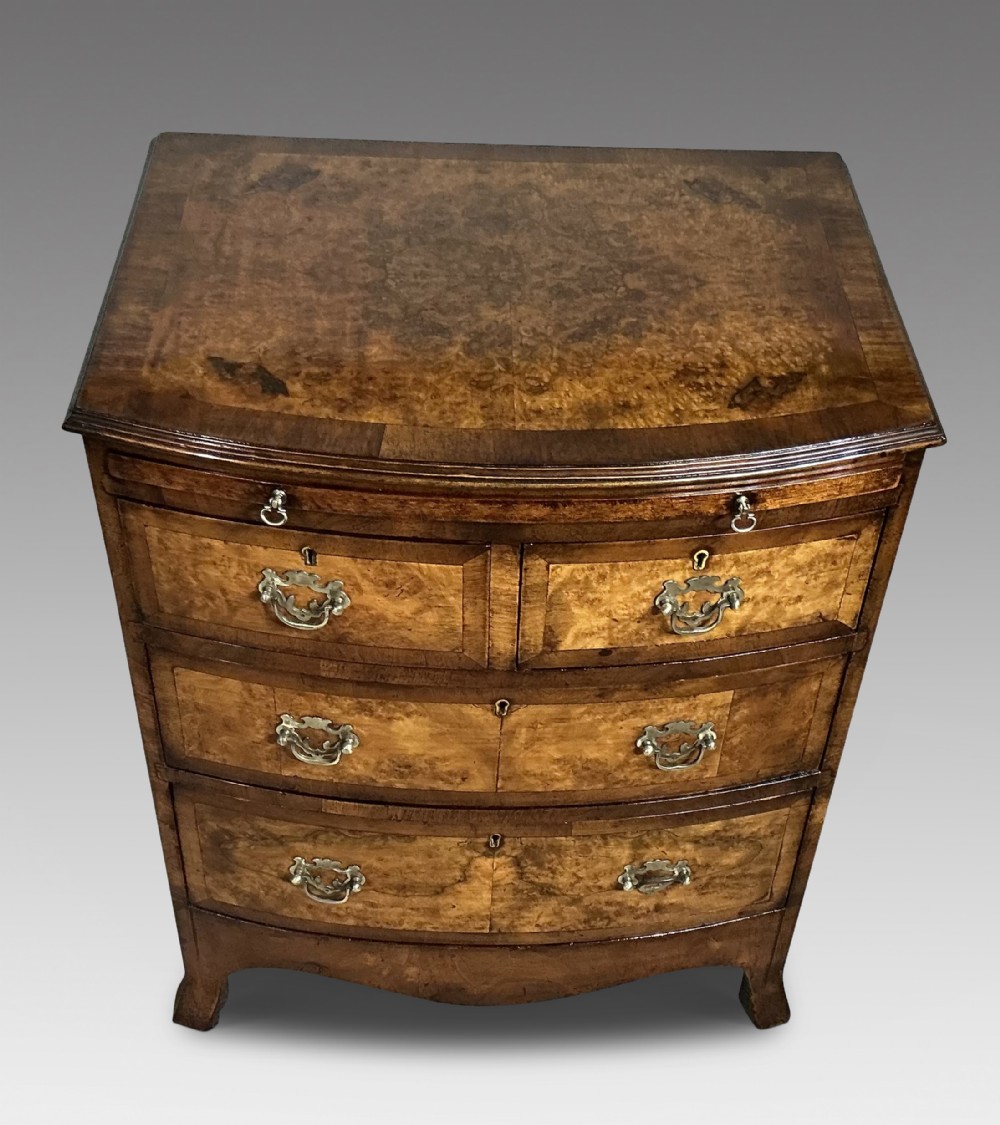 An antique burr walnut bowfront chest of drawers featuring decorative brass handles and a crossbanded top.