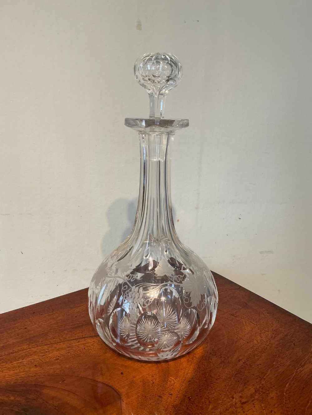 A Victorian clear cut glass decanter featuring etched grapevine motifs, starburst cuttings, a fluted neck, and a faceted glass stopper.