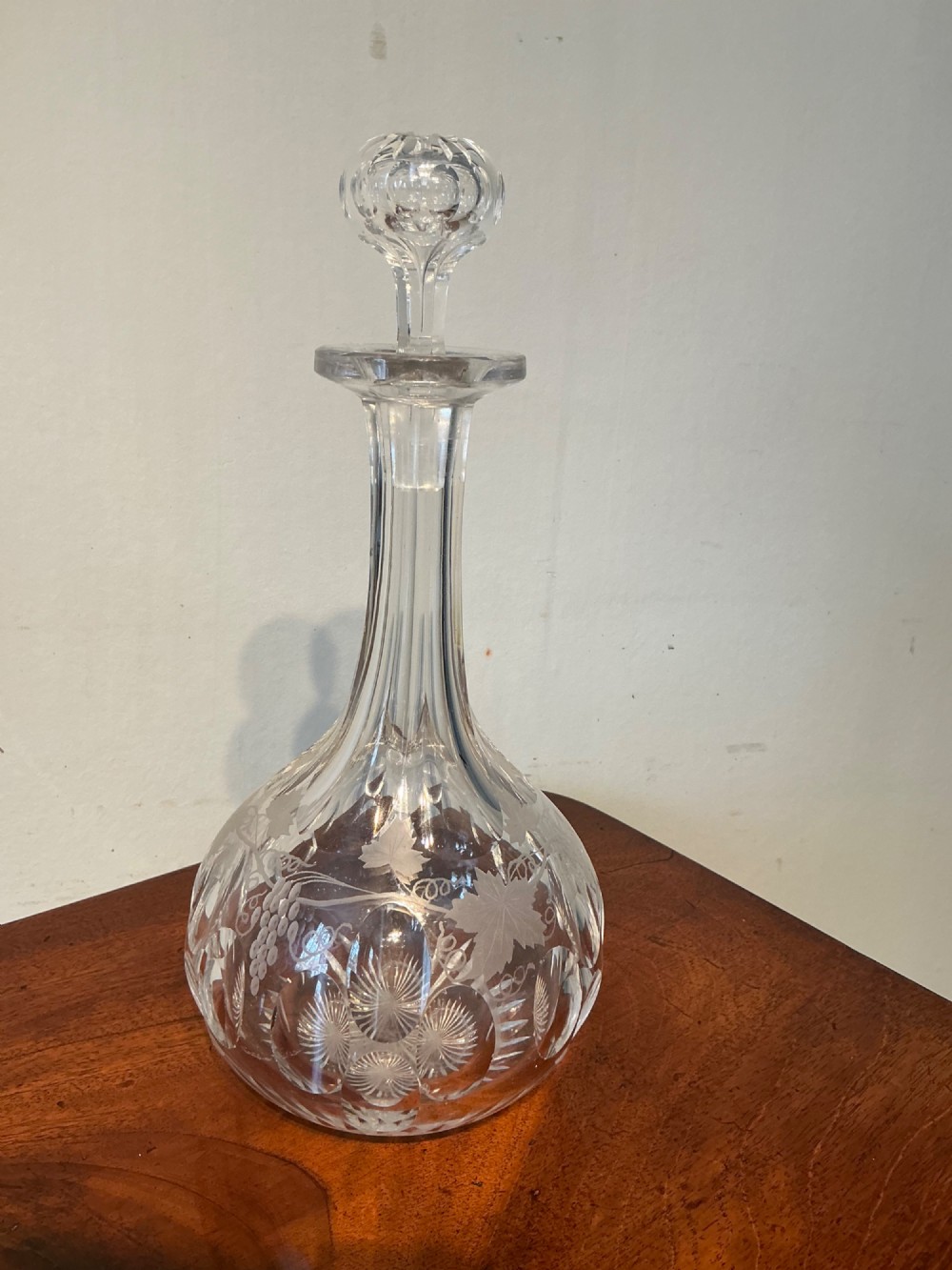 A Victorian clear cut glass decanter featuring etched grapevine motifs, starburst cuttings, a fluted neck, and a faceted glass stopper. View II