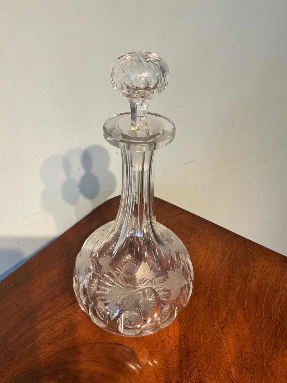 A Victorian clear cut glass decanter featuring etched grapevine motifs, starburst cuttings, a fluted neck, and a faceted glass stopper. View III