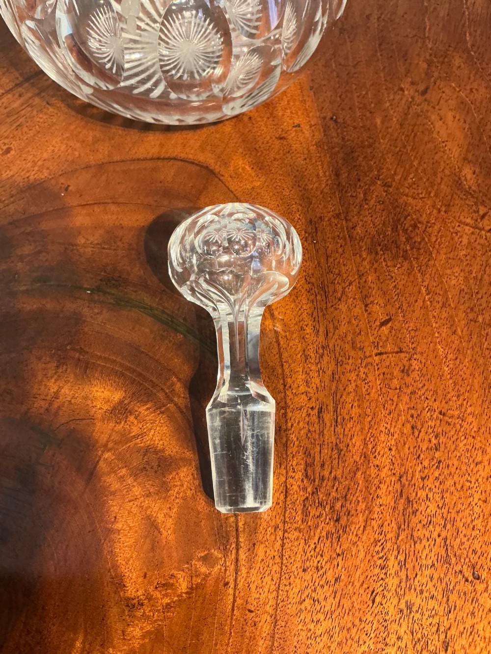 A Victorian clear cut glass decanter featuring etched grapevine motifs, starburst cuttings, a fluted neck, and a faceted glass stopper. View IV