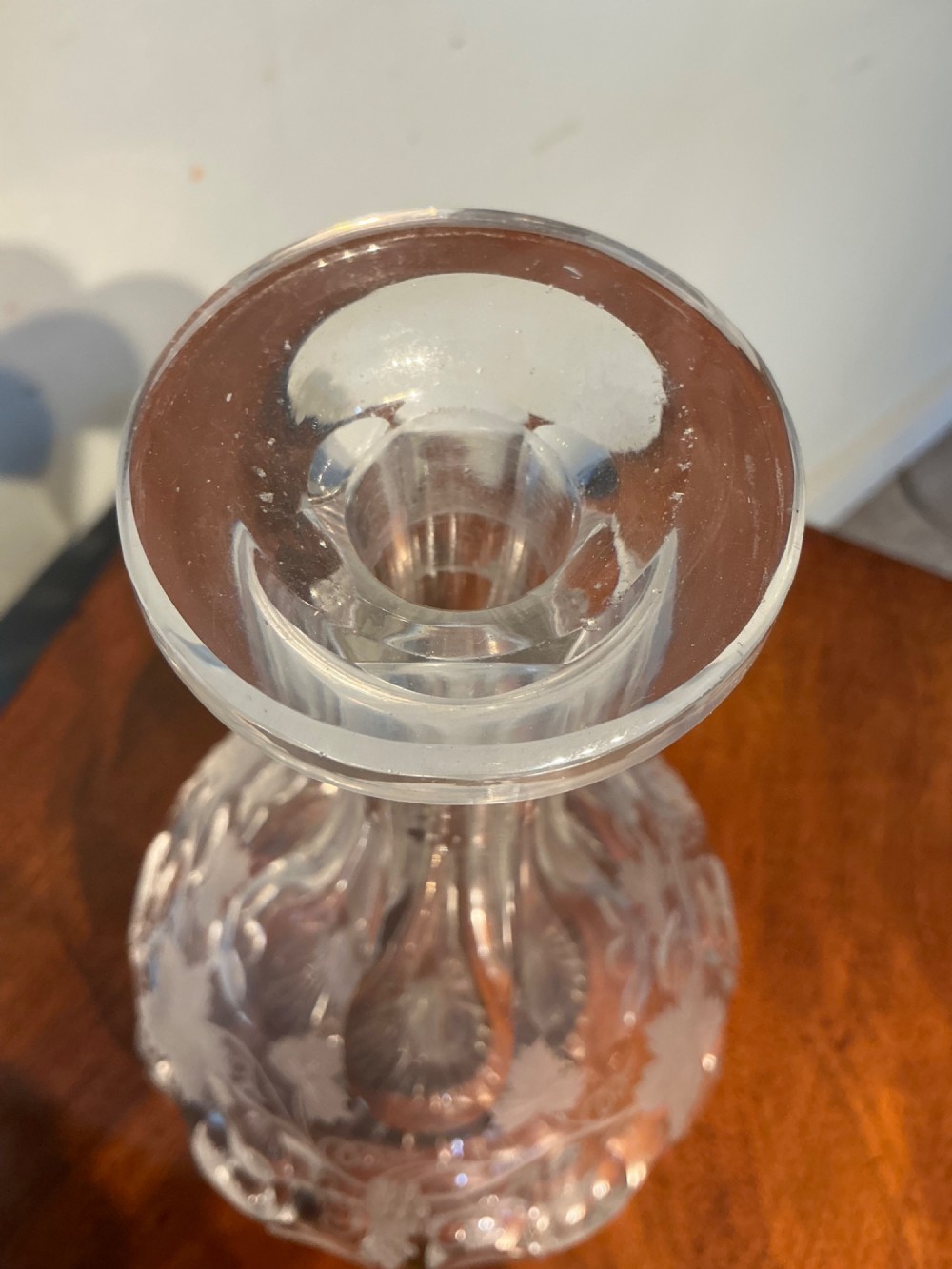 A Victorian clear cut glass decanter featuring etched grapevine motifs, starburst cuttings, a fluted neck, and a faceted glass stopper. View V