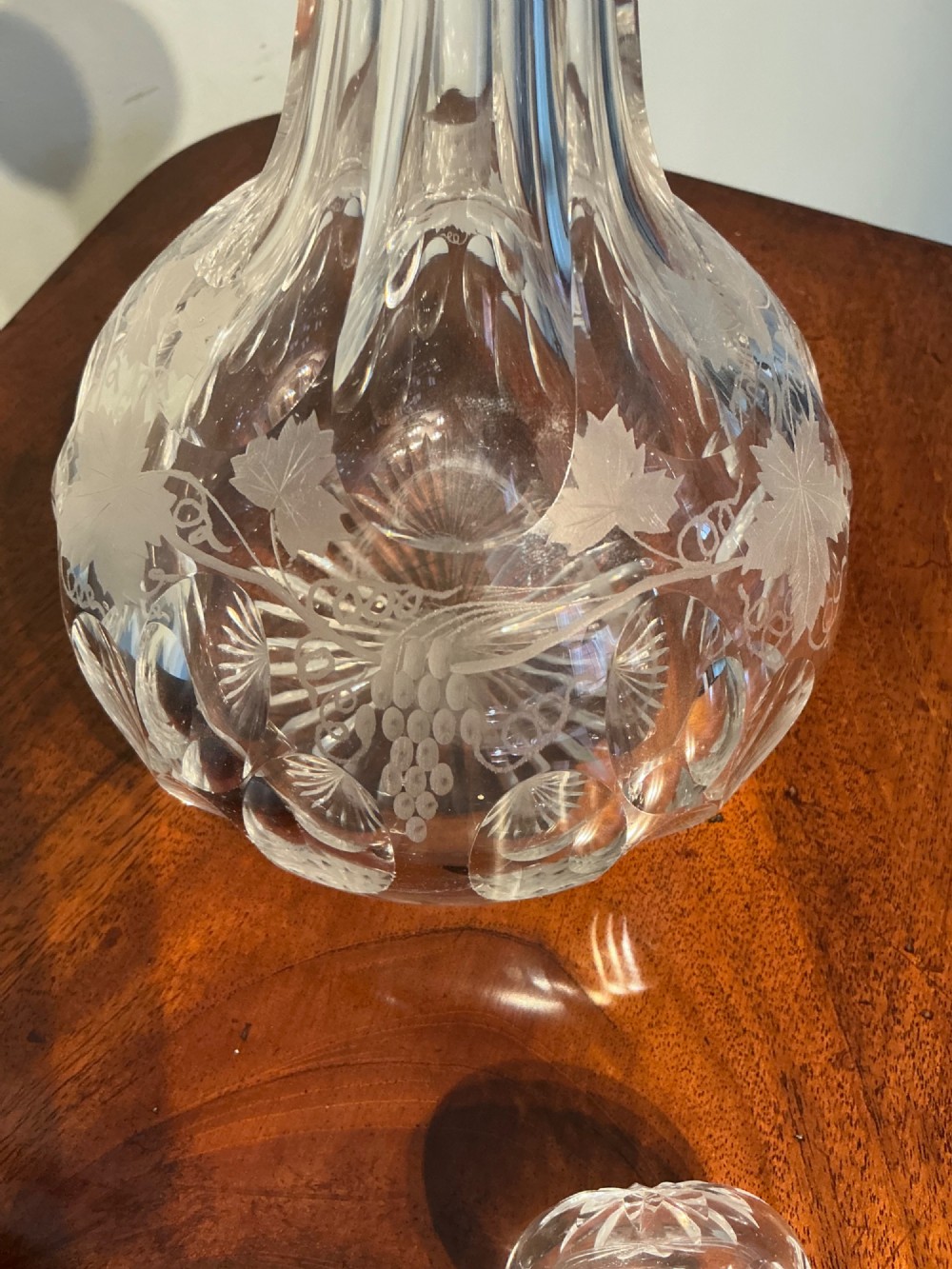 A Victorian clear cut glass decanter featuring etched grapevine motifs, starburst cuttings, a fluted neck, and a faceted glass stopper. View VI