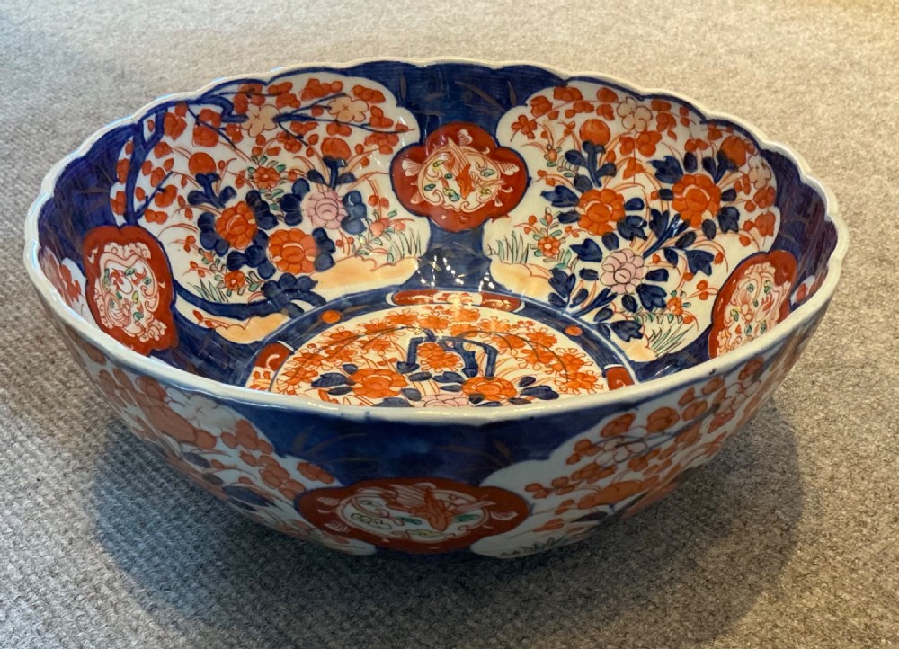 A large hand-painted Japanese Imari porcelain bowl featuring a scalloped lobed rim, floral panels, and underglaze cobalt blue and iron red patterns. View IV