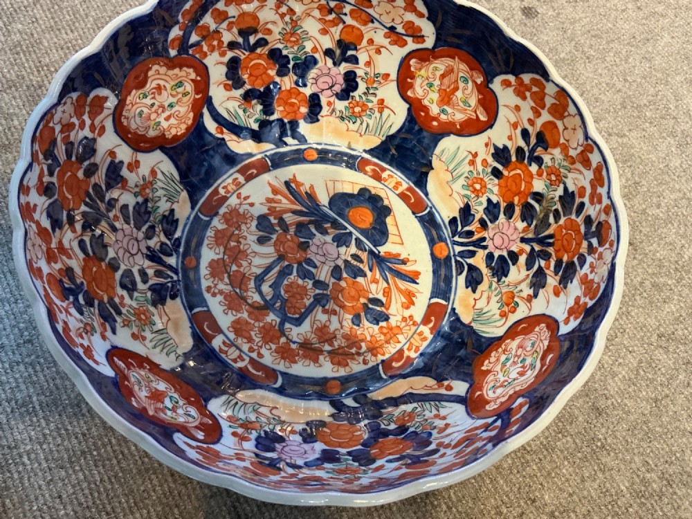 A large hand-painted Japanese Imari porcelain bowl featuring a scalloped lobed rim, floral panels, and underglaze cobalt blue and iron red patterns. View VIII