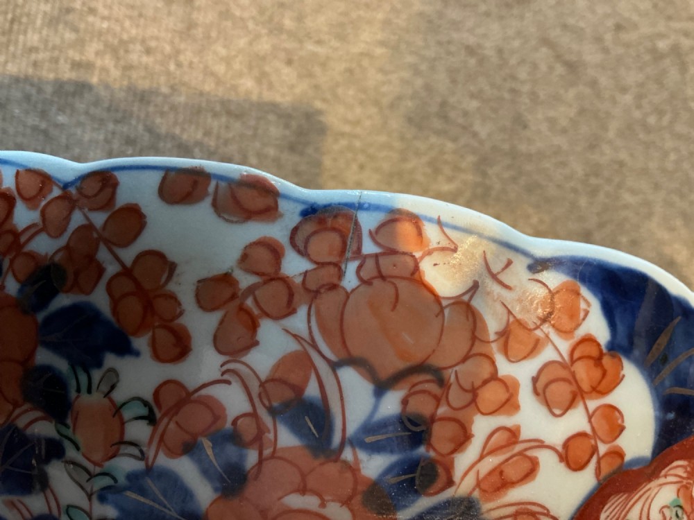 A large hand-painted Japanese Imari porcelain bowl featuring a scalloped lobed rim, floral panels, and underglaze cobalt blue and iron red patterns. View IX
